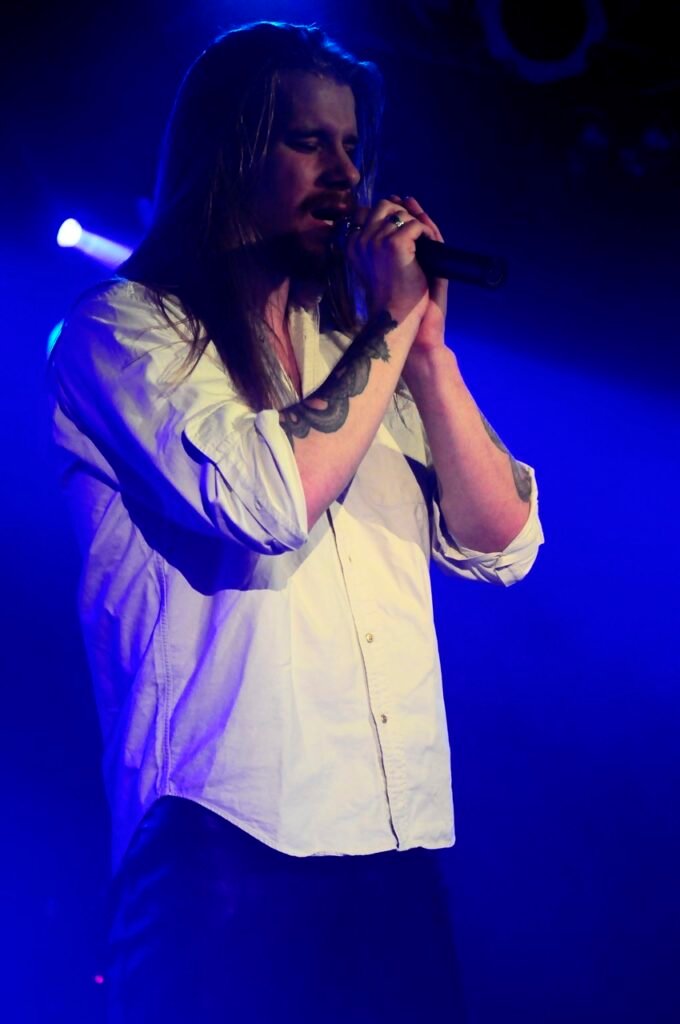 Sångaren i bandet seventh dimension. vit skjorta, långt hår och tatueringar på armarna