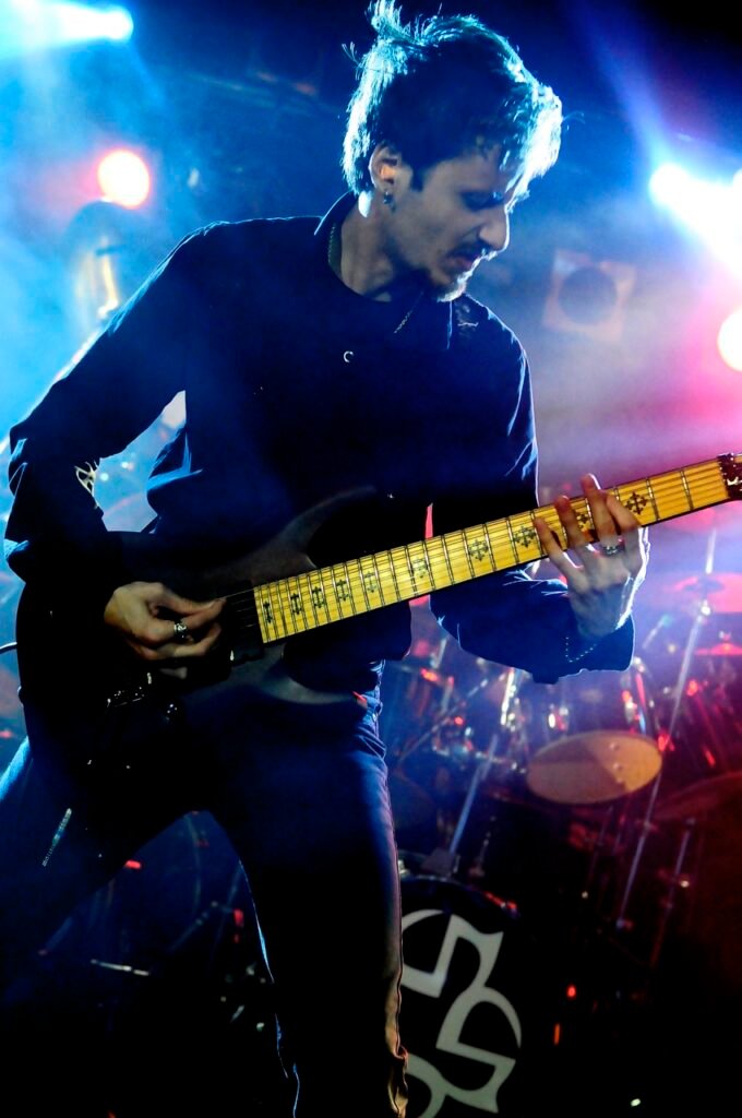 Guitaristen i Seventh Dimension. Svarta kläder, kortare hår, svart guitarr.