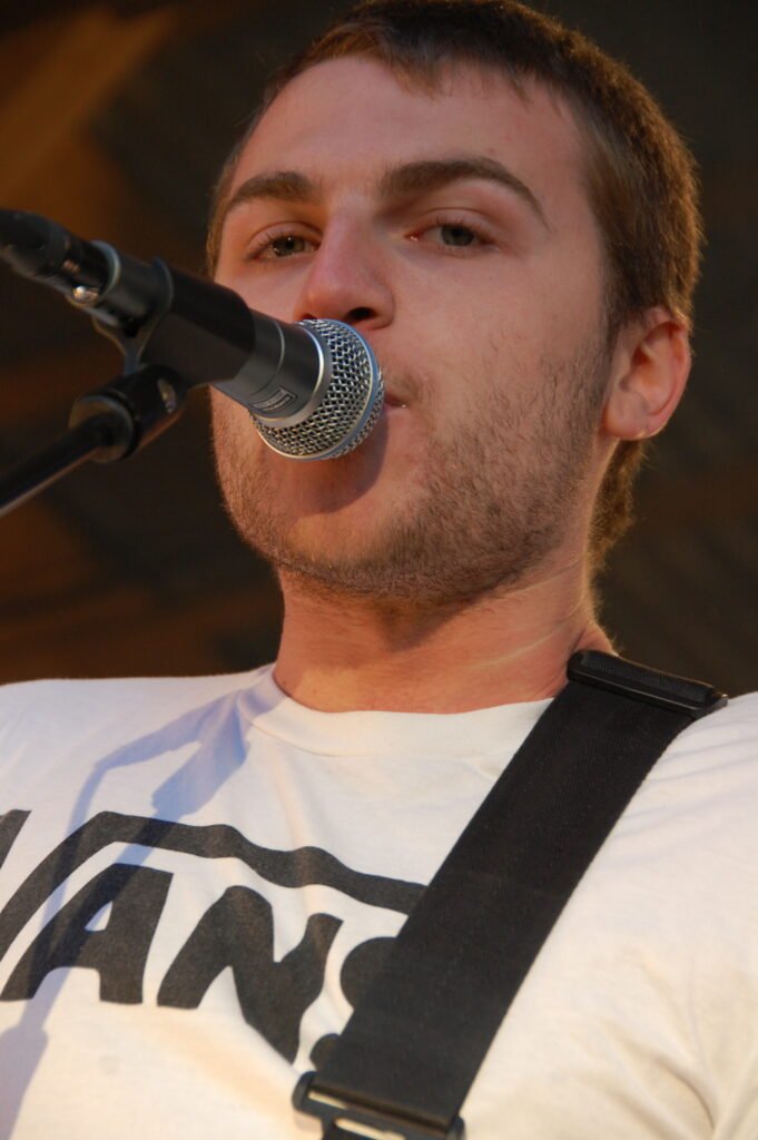 Sångare i vit vanströja och kort hår, tittar in i micen.