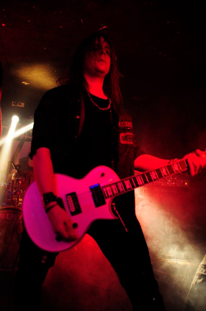 guitarist med långt hår och vit gitarr.