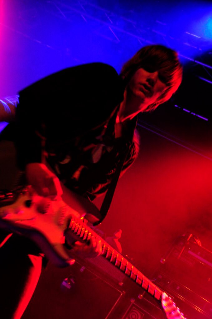 Guitarist med svarta kläder, tittar in i kameran, 50 tals frisyr.